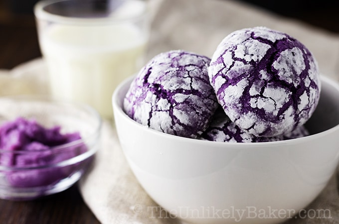 Ube crinkle cookies in a bowl with a glass of milk in the background.