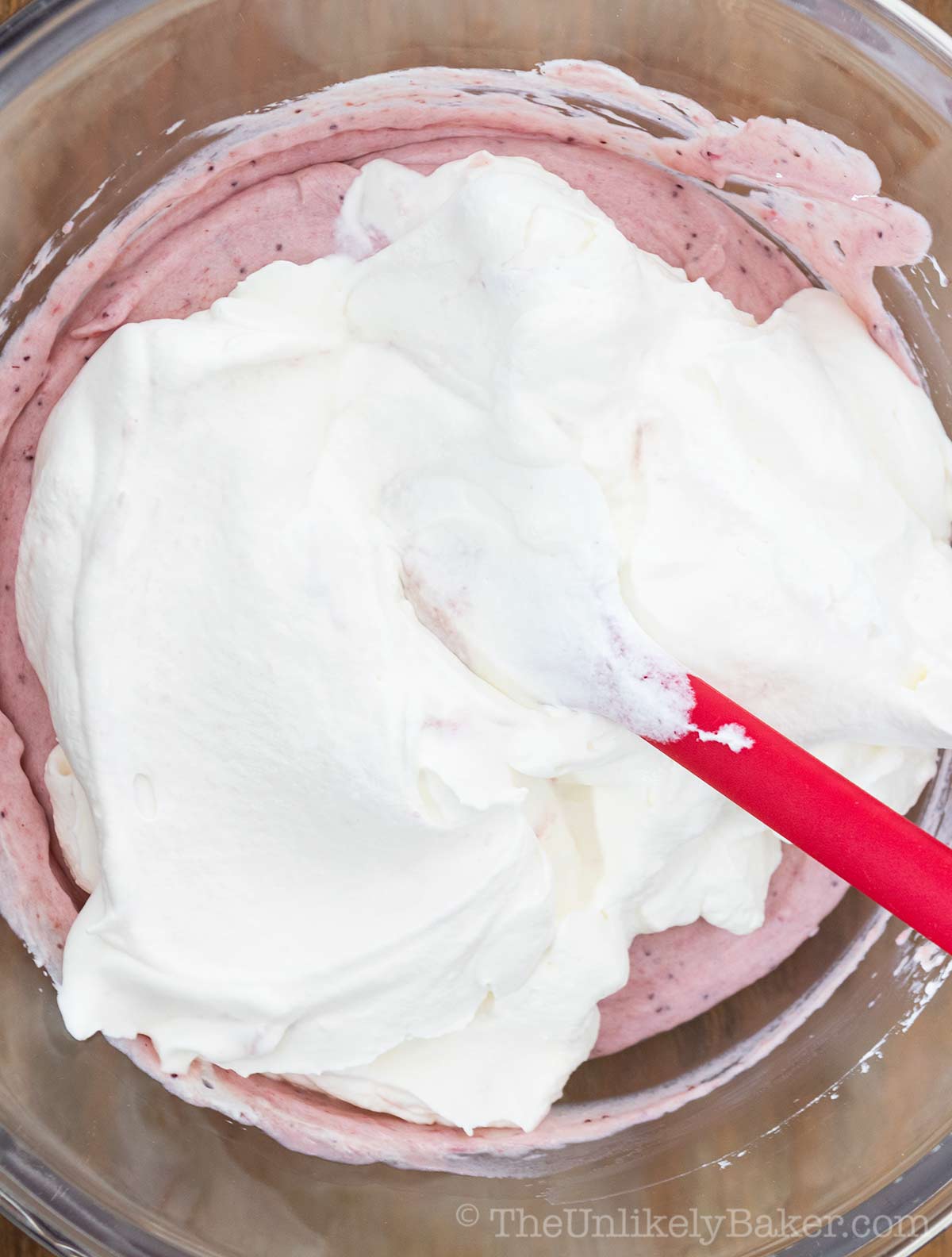 Whipped cream being folded into strawberry mixture.