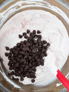 Chocolate chips being stirred into strawberry ice cream.