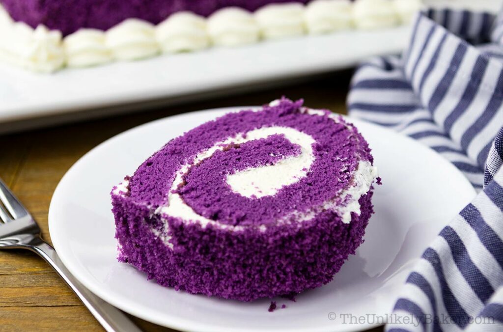 Slice of ube roll cake on a white plate.