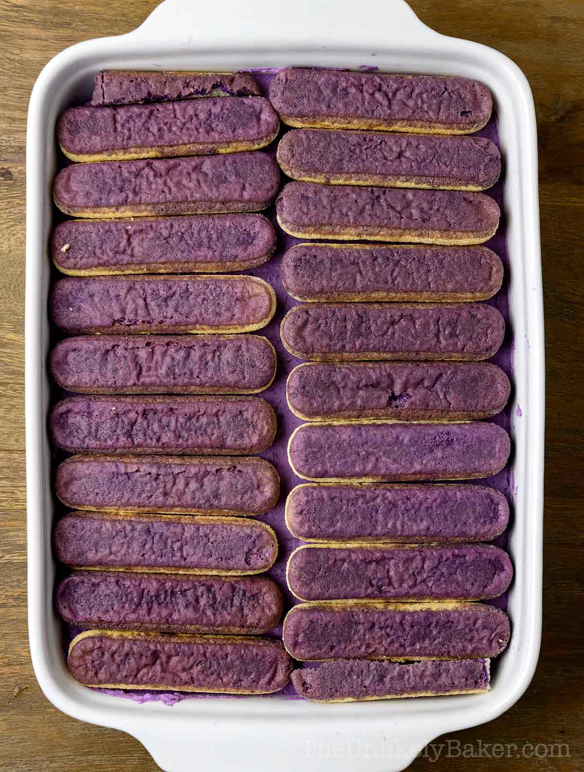 Ladyfinger cookies dipped in ube syrup placed on a baking dish.