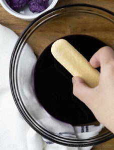 Dipping a ladyfinger cookie in ube syrup.