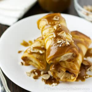 A stack of apple spring rolls with caramel sauce and chopped almonds.