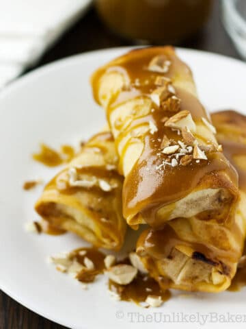 A stack of apple spring rolls with caramel sauce and chopped almonds.