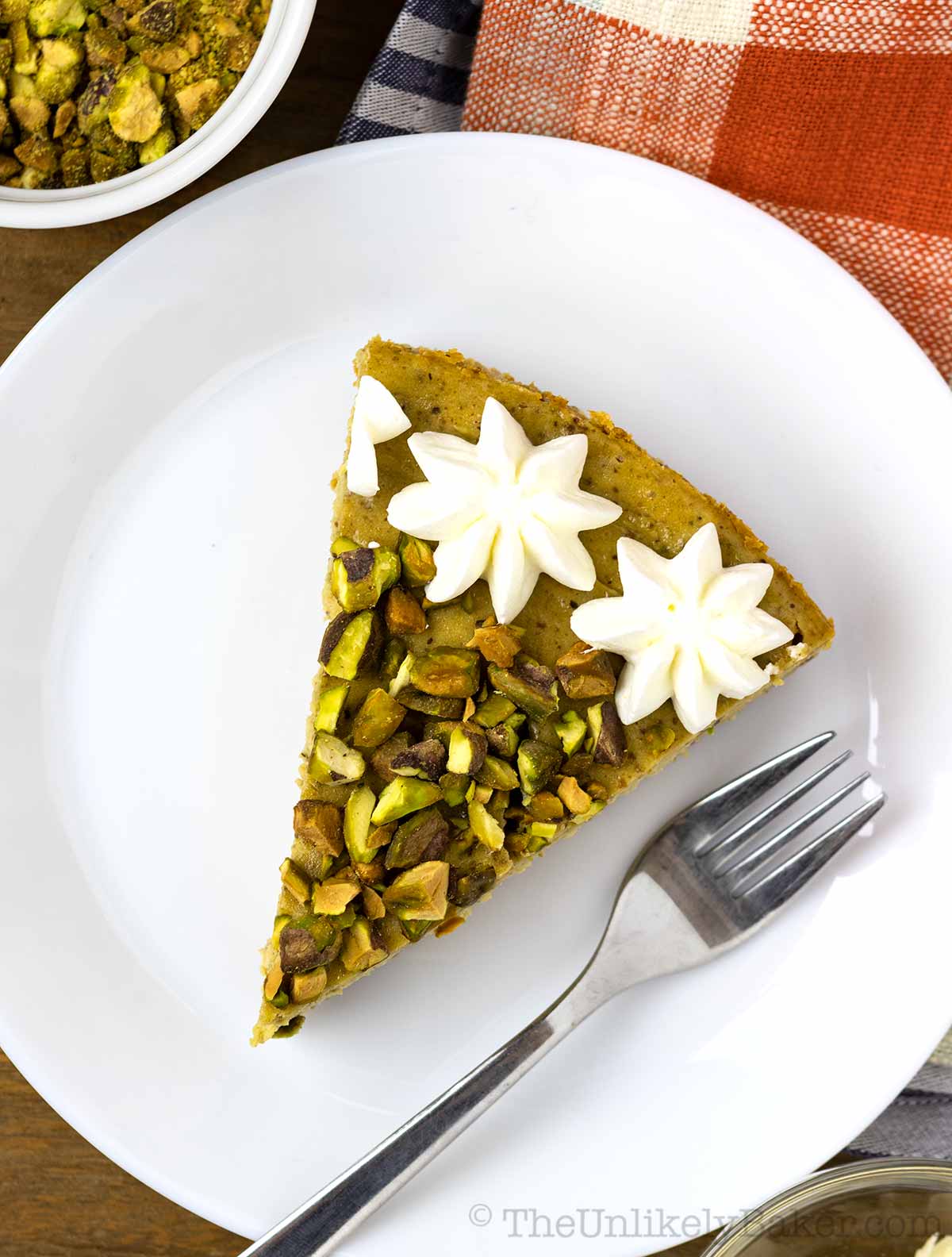 Slice of cheesecake with pistachios and whipped cream on a plate.