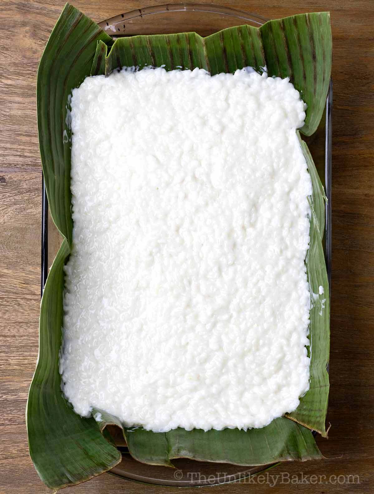 Cooked glutinous rice in a baking dish lined with banana leaves.