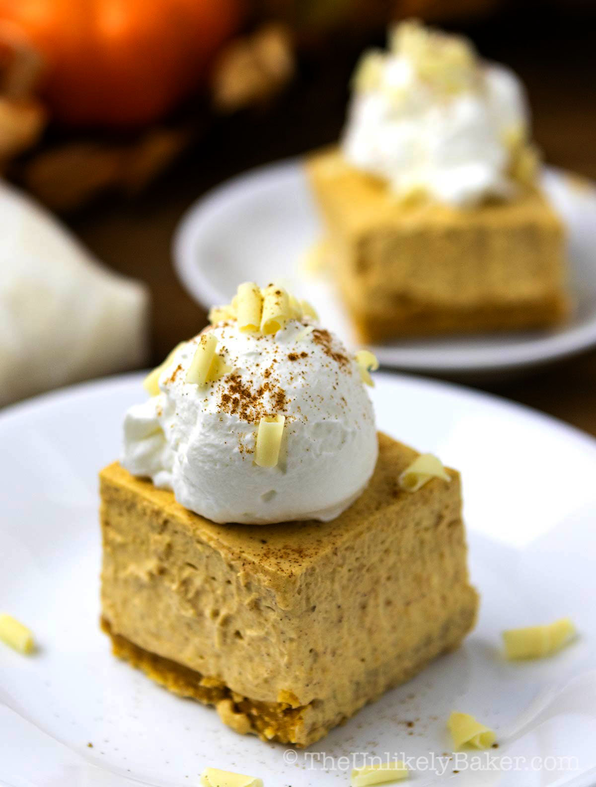 A piece of pumpkin cheesecake no bake bars with whipped cream topping and sprinkled with pumpkin spice.