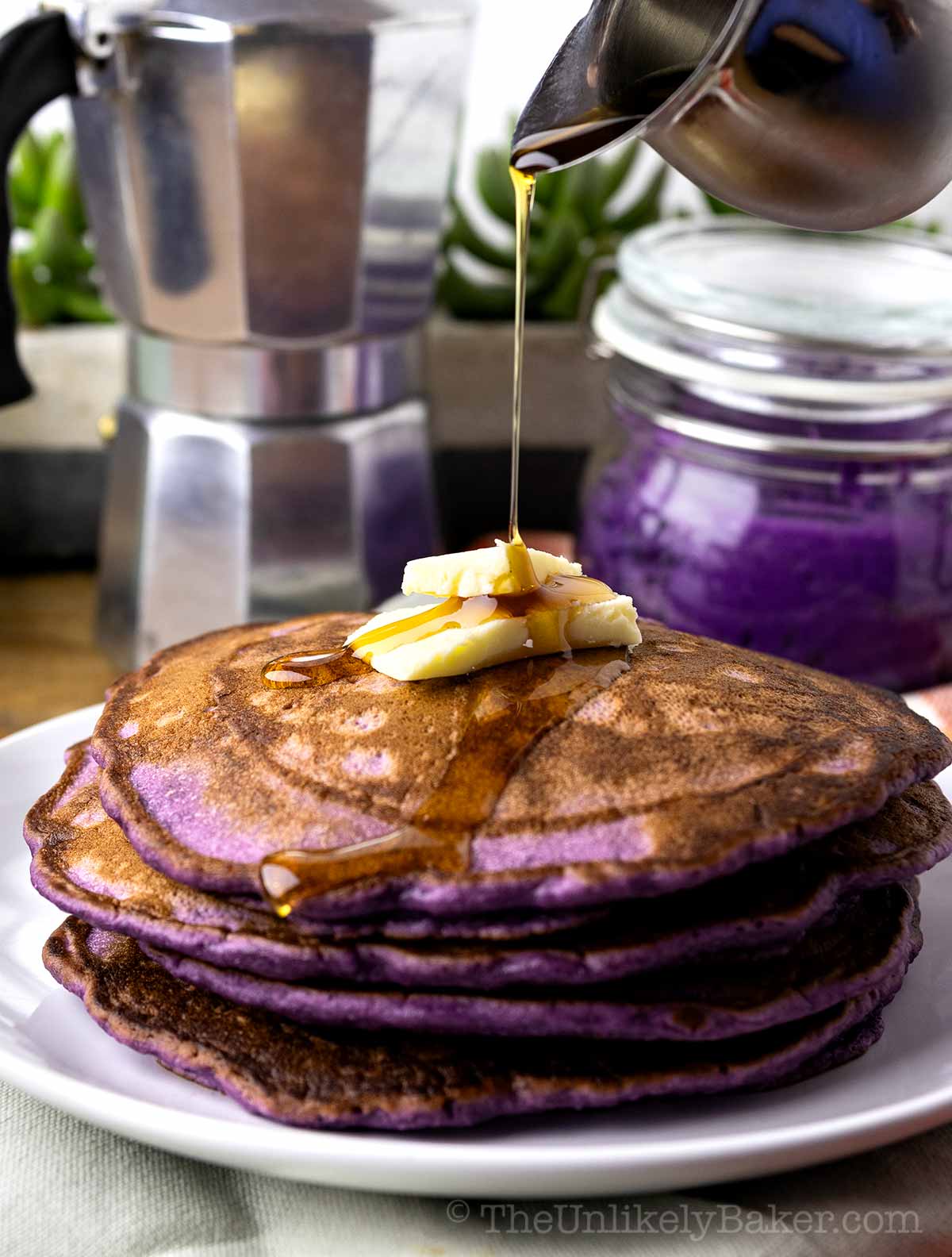 A stack of ube pancakes drizzled with maple syrup.