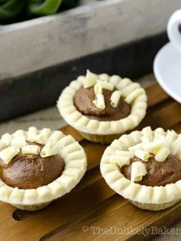 Mini chocolate tarts with shaved white chocolate on top.