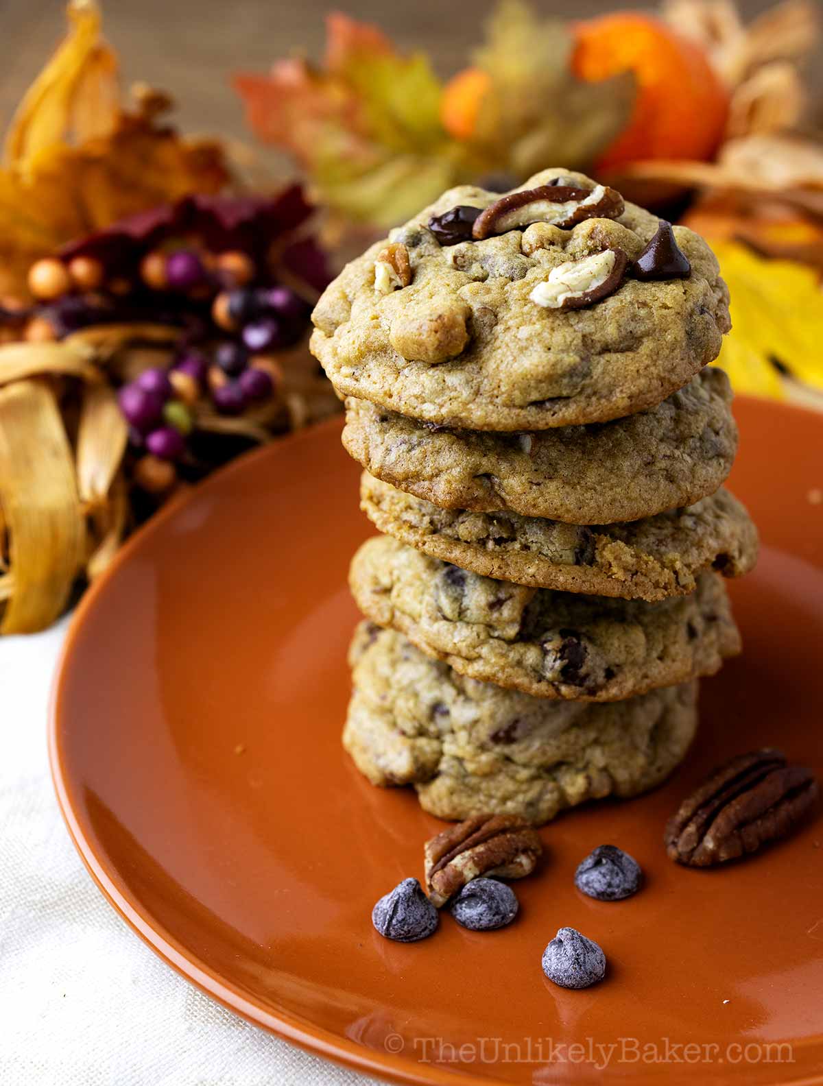 A stack of choco chip pecan cookies with Thanksgiving decor in the background.