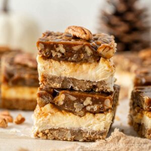 Slices of pecan pie cheesecake bars showing graham cracker crust, cheesecake layer and pecan pie topping.
