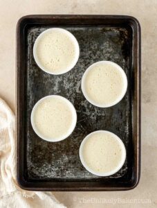 Creme brulee in ramekins on a baking pan.